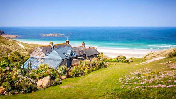 A coastal house with a sloped roof, a conservatory, and a view of the ocean and beach. - Castaways, Vellandreath Cornish Cottages (Sennen)