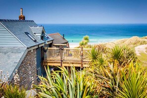 A coastal property with a stone building, a wooden deck, and a view of the ocean. - Sandpipers, Beach Cottage, Great Sea Views, Patio (Sennen)