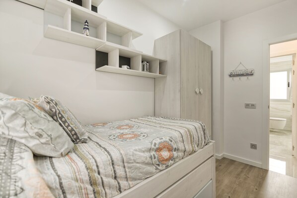 A bedroom with a bed, built-in shelving, a wardrobe, and a bathroom visible through an open door.