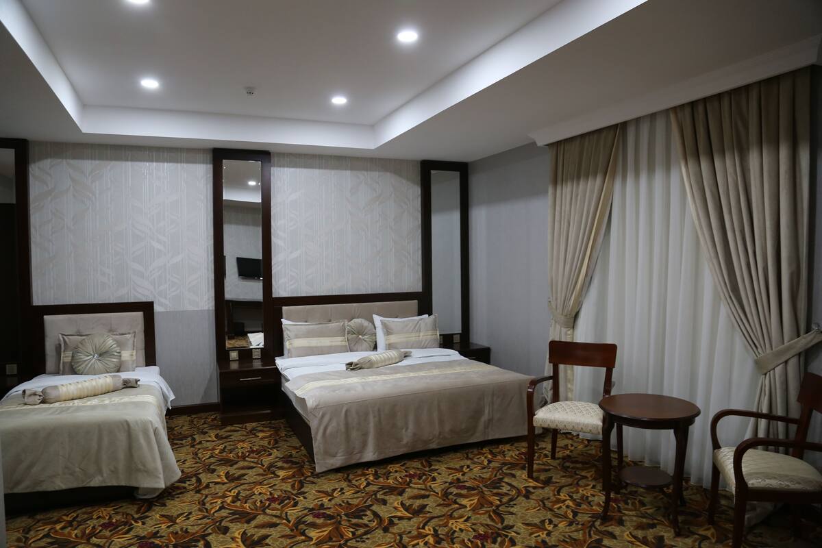 A hotel room with a large bed, two smaller beds, a desk, and a chair.