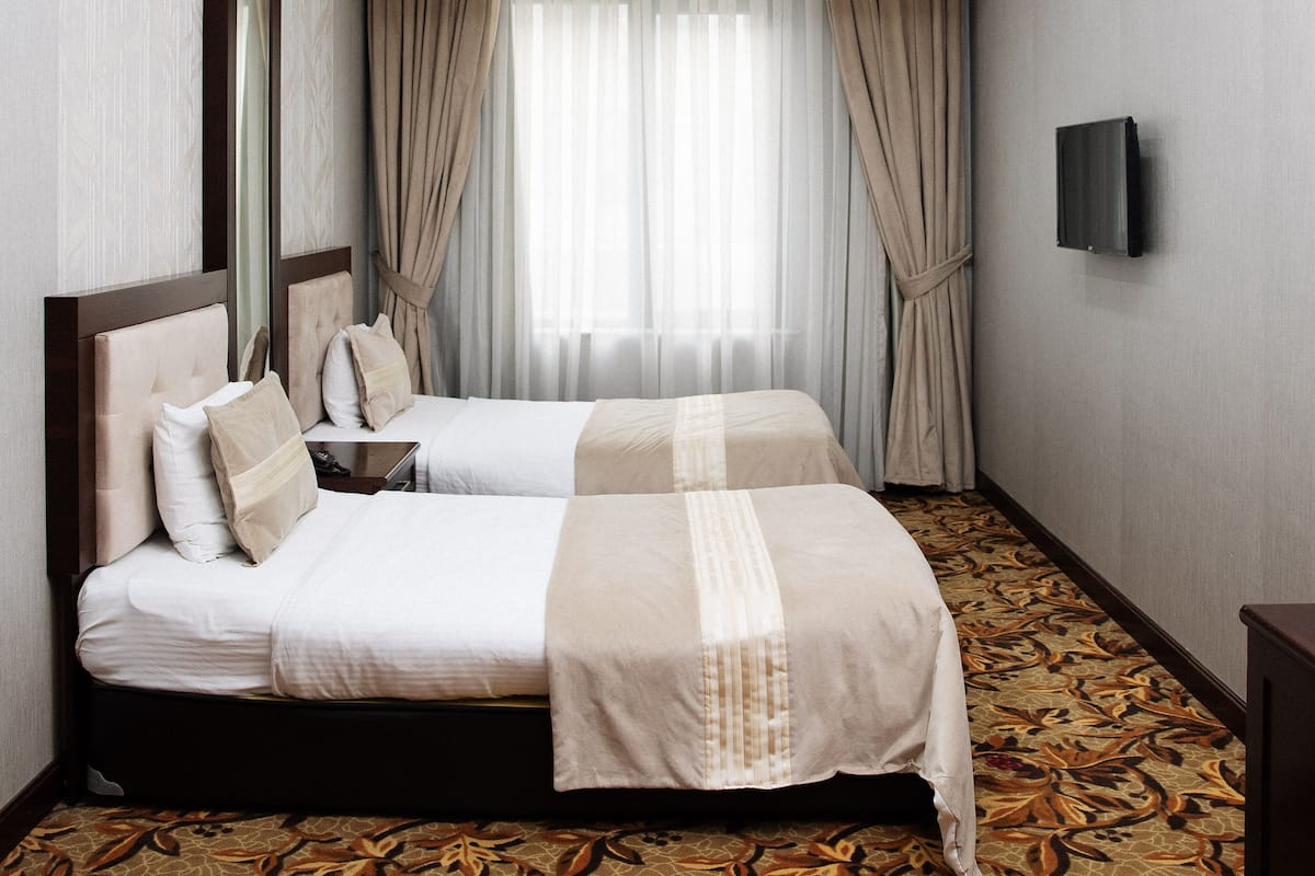 A hotel room with two beds, a TV on the wall, and a large window with curtains.
