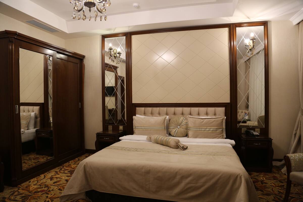 A hotel room with a large bed, a wardrobe, a mirror, and a chandelier.