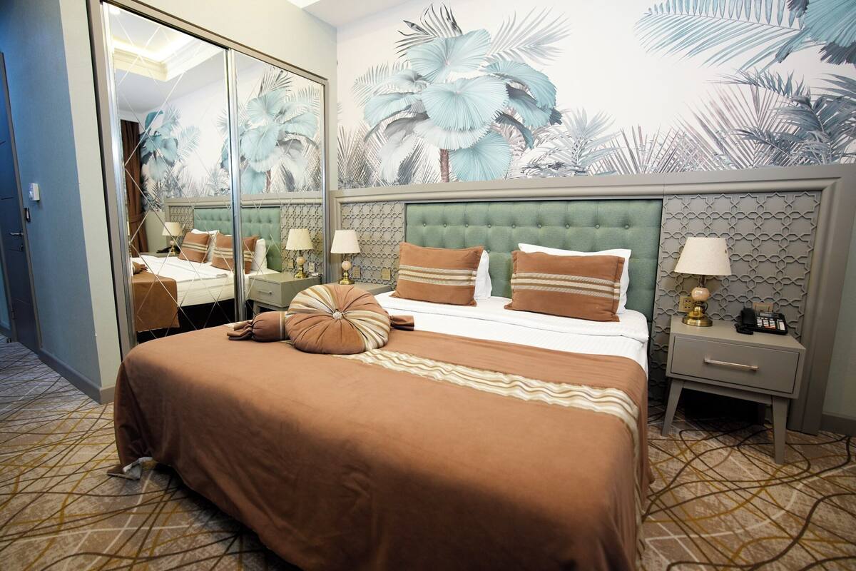A hotel room with a large bed, a nightstand, a mirror, and a wall with a tropical mural.