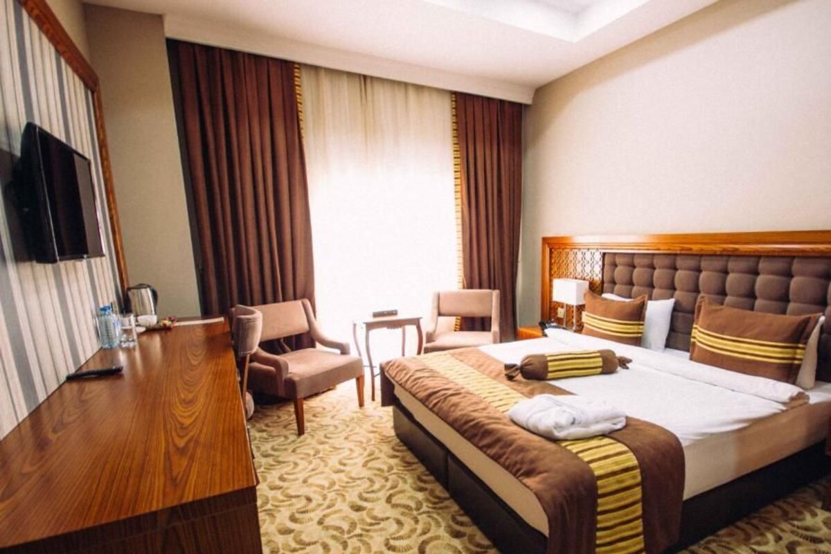 A hotel room with a large bed, a wooden desk, a television, and a seating area with two chairs.