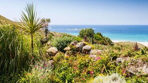 A coastal garden with a variety of plants and rocks, leading to a beach. - Whitebreakers, Beach Cottage, Sea-views, Garden (Sennen)