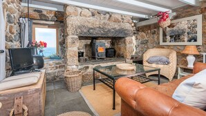 A cozy living room with a stone fireplace, comfortable seating, and a television. - Whitebreakers, Beach Cottage, Sea-views, Garden (Sennen)
