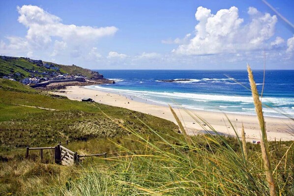 Un paysage côtier avec une plage, des zones herbeuses et un ciel dégagé.