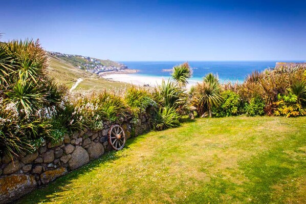 A coastal landscape with a stone wall, grassy area, and a view of the beach and ocean. - Beach Cottage, Sea views, Garden, Amazing Location (Sennen)