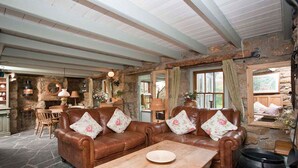 A rustic living room with stone walls, a wooden ceiling, and leather sofas with floral cushions. - Petra, Beach Cottage, Great Sea Views, Garden (Sennen)