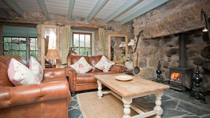 A cozy living room with a stone fireplace, leather sofas, and a wooden coffee table. - Petra, Beach Cottage, Great Sea Views, Garden (Sennen)