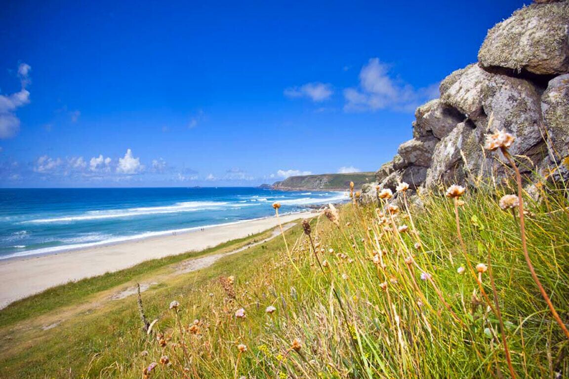 Eine Küstenlandschaft mit Strand, Grasflächen und Felsformationen.