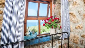 Eine Steinsäule mit Fenster, ein Blumentopf mit roten Blüten und ein blaues Bootsmodell.