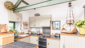 A kitchen with white cabinets, a black stove, and a hanging light fixture. - Girl Annie, Beach Cottage, Great Sea-Views, Garden (Sennen)