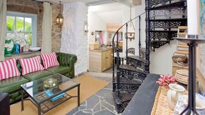 Una sala de estar acogedora con un sofá verde, una mesa de centro de cristal y una escalera espiral negra.