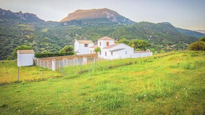 Un edificio bianco con tetto rosso, circondato da un recinto bianco, sullo sfondo di montagne.