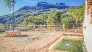 Un cortile con piscina in mattoni, recinzione bianca e una montagna sullo sfondo.