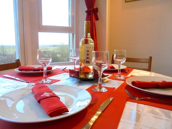 A dining table set with red napkins, wine glasses, and a bottle of wine.