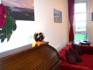 A living room with a wooden bench, a red sofa, a glass vase, and a painting on the wall.