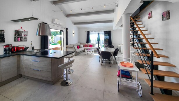 A modern kitchen with a central island, a dining area with a round table, and a staircase with wooden steps. - Amazing home in Callian (Callian)