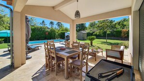 A covered patio with a pool, wooden furniture, and a grill area. - Amazing home in Callian (Callian)