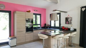 A modern kitchen with a pink accent wall, built-in ovens, a bar area with stools, and a window providing natural light. - Amazing home in Callian (Callian)