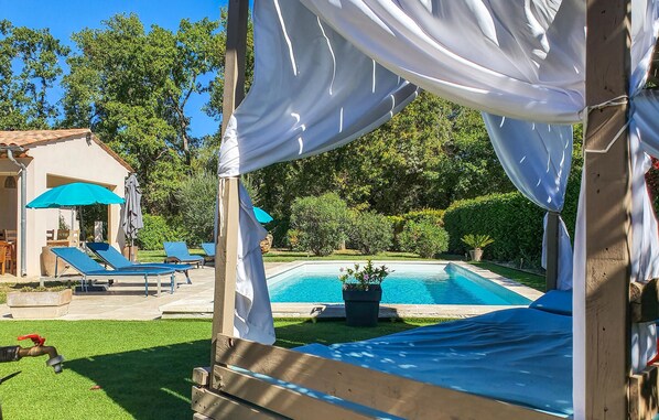 A covered outdoor area with a pool, lounge chairs, and a pergola with white drapes.