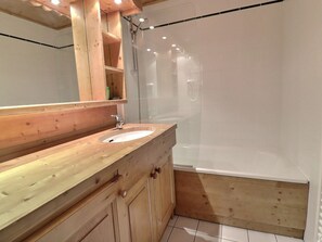 A modern bathroom with a wooden vanity, a sink, a mirror, and a glass-enclosed shower area. - Charming apartment in Méribel for 4 people - Pets allowed (Méribel)