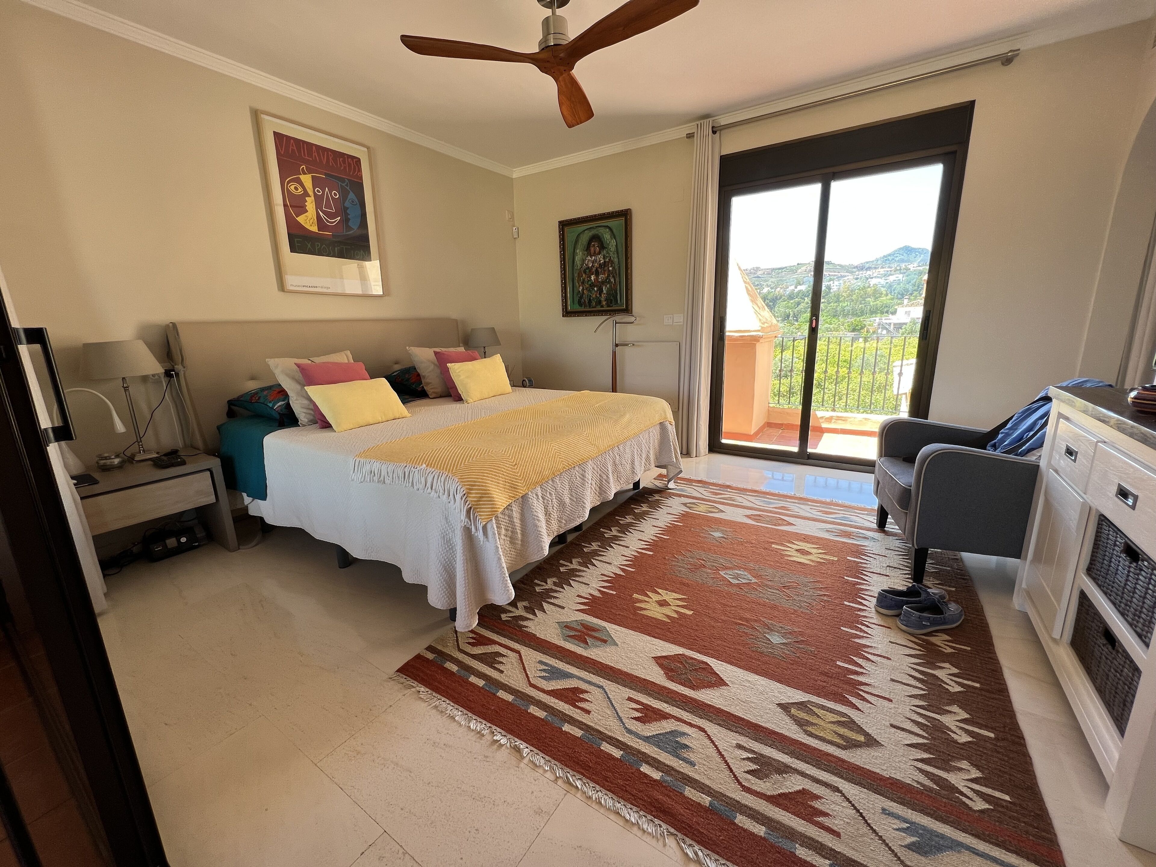 Un dormitorio con cama, mesita de noche, lámpara y vistas al exterior a través de una puerta corredera.