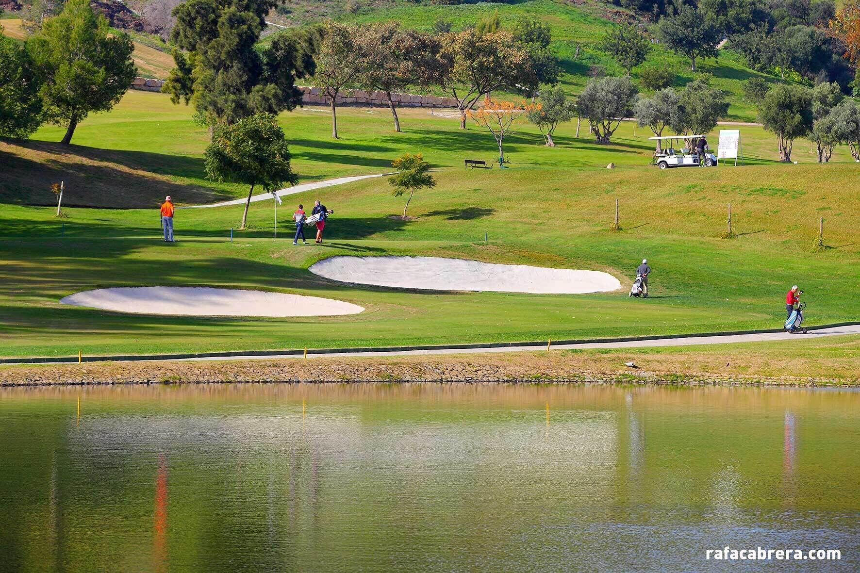 Ein Golfplatz mit Sandbunkern, einem Teich und einem Wanderweg.