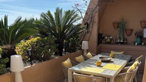 An outdoor patio with a tiled table and chairs, surrounded by plants and a decorative wall. - LUXURY MARBELLA DUPLEX OF 3 CH - 3 SDB - OF 155 M² + TERRACES 100 M²  (estepona)