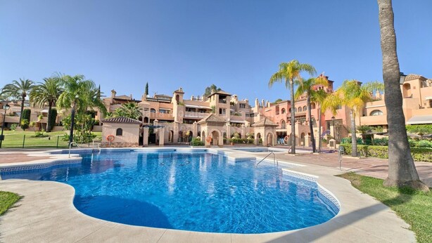 A swimming pool surrounded by a resort with Mediterranean-style architecture, palm trees, and a clear sky. - LUXURY MARBELLA DUPLEX OF 3 CH - 3 SDB - OF 155 M² + TERRACES 100 M²  (estepona)