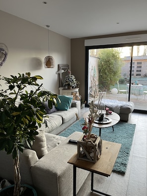 Un salon moderne avec un canapé, une table basse et une grande fenêtre donnant sur l’extérieur.