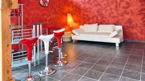 A modern living room with a white sofa, red and white bar stools, a round table, and a lamp. - Homerez - Comfortable Apartment with Garden (Saint-Dié-des-Vosges)