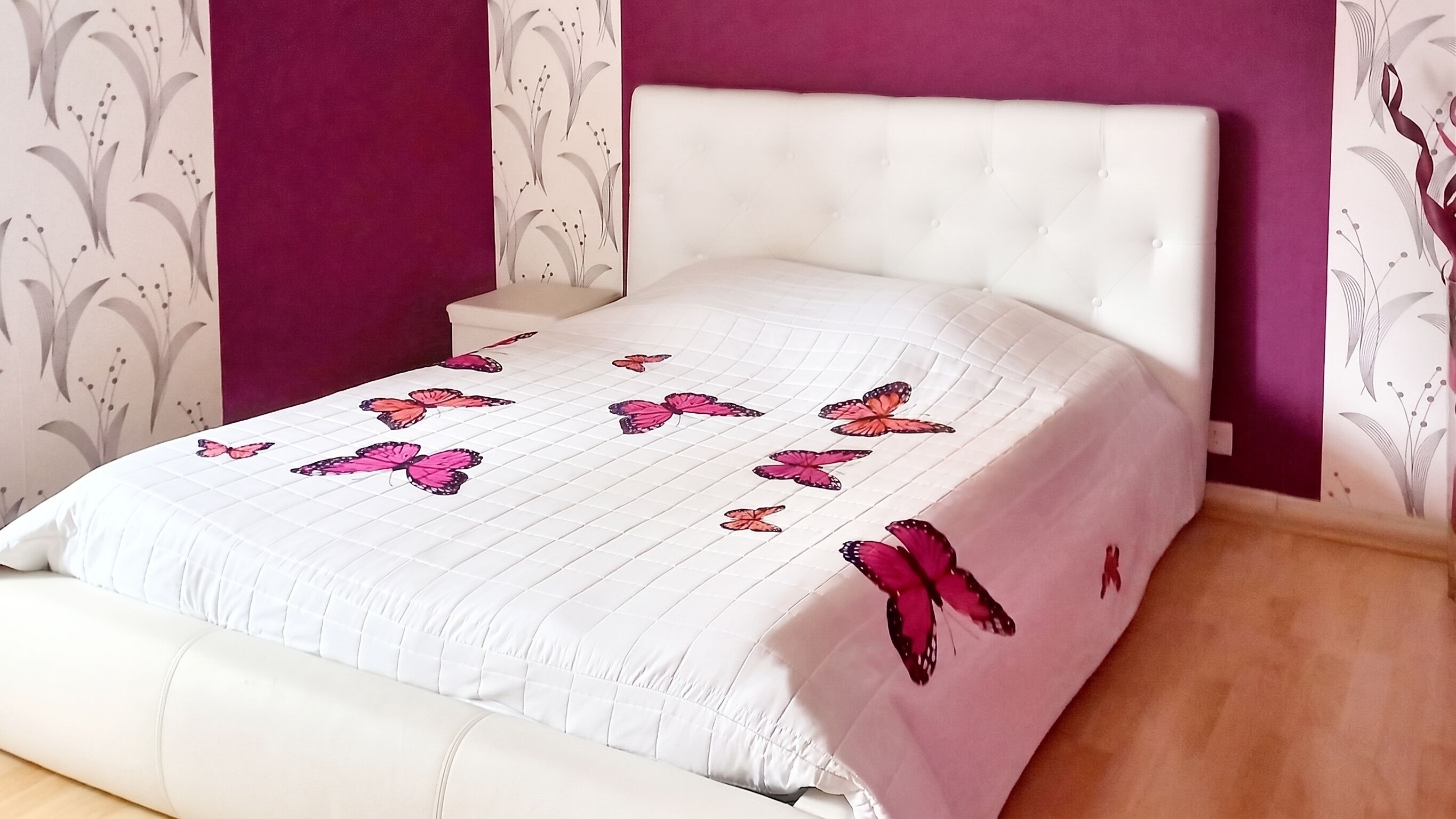 A bed with a white headboard and a quilt with pink butterflies.