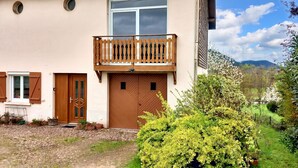 A two-story building with a balcony, a brown door, and a small garden area. - Homerez - Comfortable Apartment with Garden (Saint-Dié-des-Vosges)