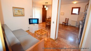 A compact living space with a sofa, a dining table, and a television. - Lignano Exclusive With Pool (Lignano Sabbiadoro)