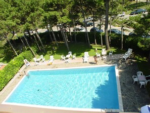 A rectangular swimming pool with clear blue water, surrounded by white lounge chairs and a stone deck. - Lignano Exclusive With Pool (Lignano Sabbiadoro)