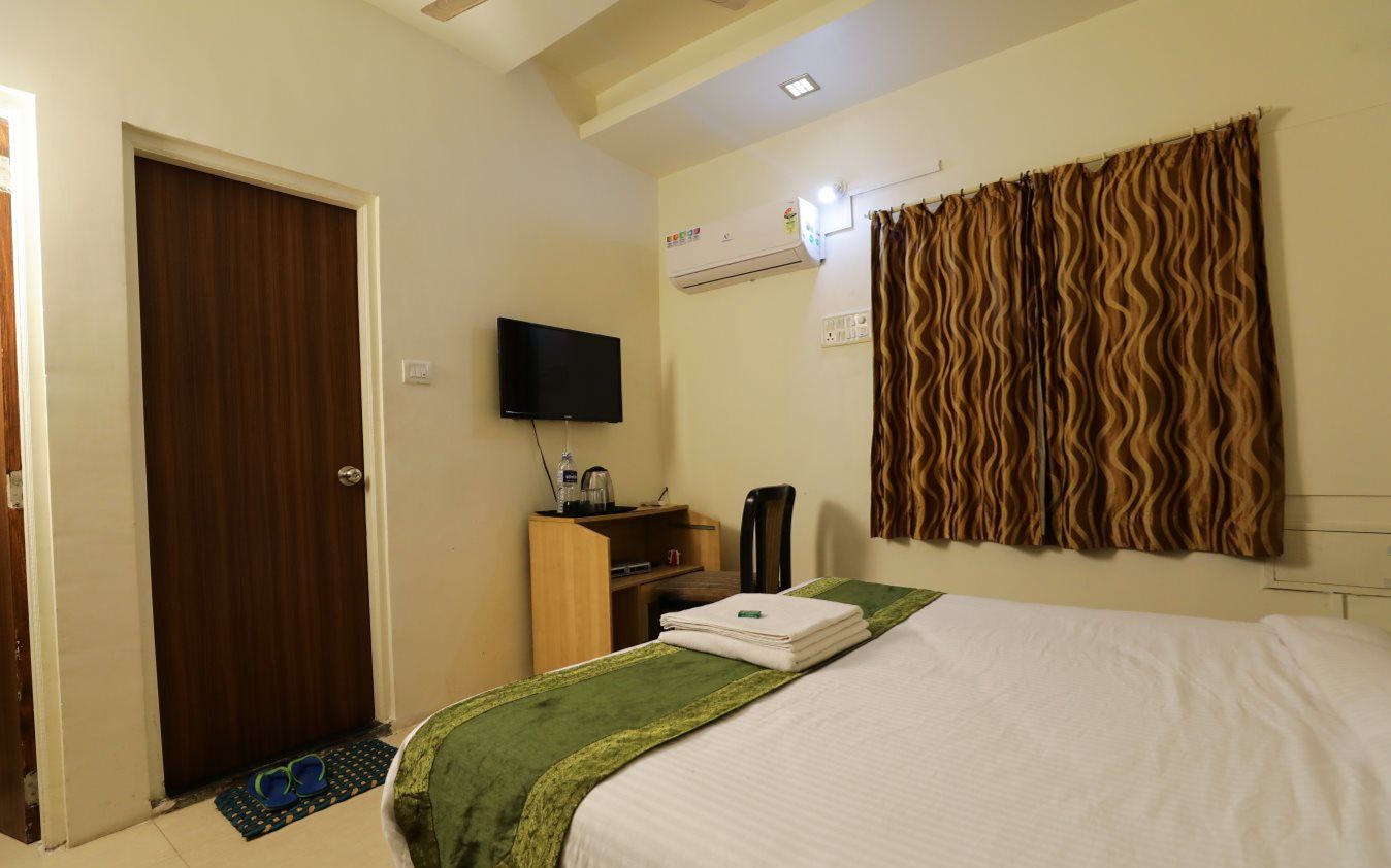 A hotel room with a bed, a television, a wardrobe, and a desk with a chair.