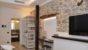 A modern hotel room with a stone wall, a flat-screen TV, a desk, and a large wardrobe. - Civico29 B&B (Como)