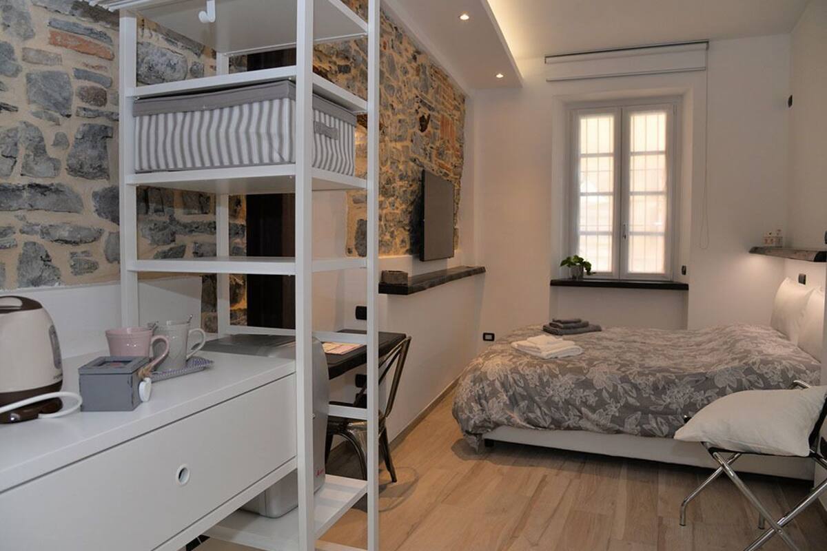 Ein Schlafzimmer mit Etagenbett, Schreibtisch mit Stuhl, Bett mit floralem Überwurf, Steinwand und Fenster mit Jalousien.