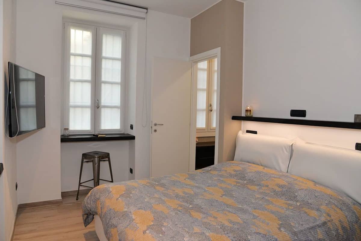Ein Schlafzimmer mit Bett, Wandfernseher, Fenster und Tür.