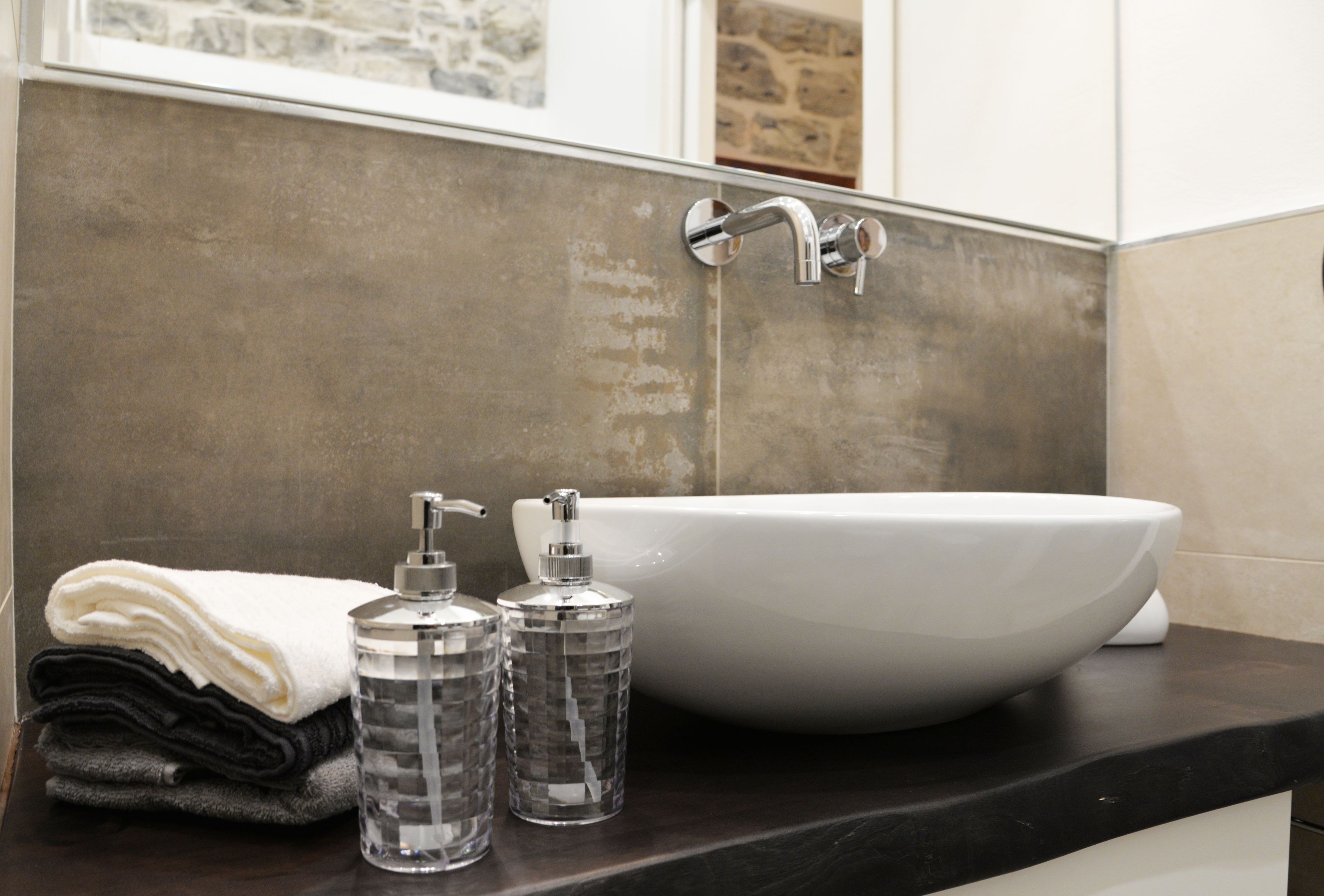 Un bagno con un lavandino bianco, un mucchio di asciugamani e due dispenser trasparenti su un piano d'appoggio scuro.