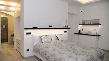 A modern bedroom with a large bed, a built-in bench, a small kitchenette, and a walk-in closet.