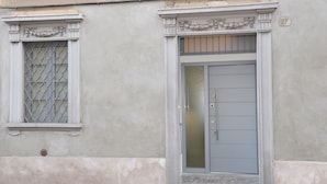A building facade with a gray door and a window with a metal grille. - Civico29 B&B (Como)
