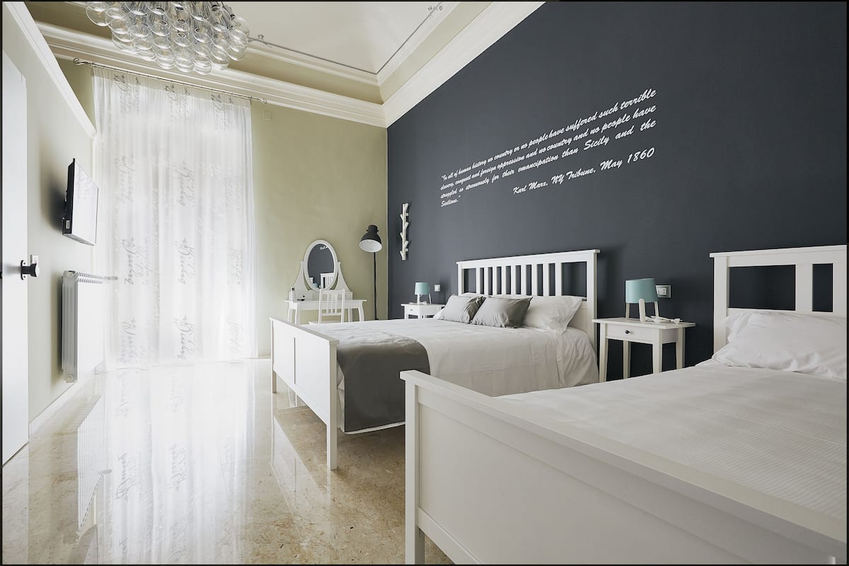 Een moderne slaapkamer met een groot bed, nachtkastjes, een spiegel en een citaat op de muur.