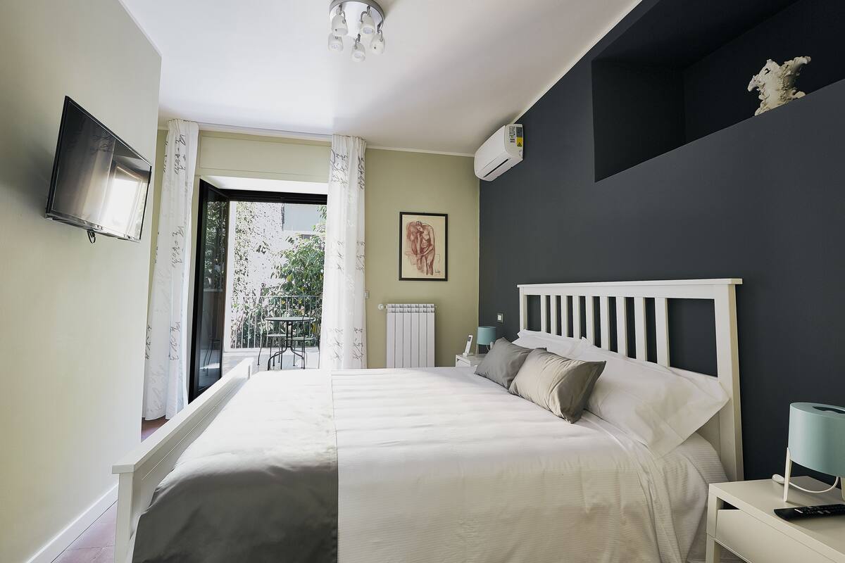 Een slaapkamer met een bed, nachtkastje en een aan de muur bevestigde televisie.
