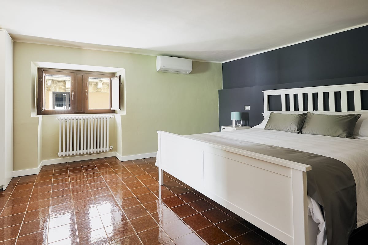Een slaapkamer met een bed, een radiator, een raam en een wandgemonteerde airconditioner.
