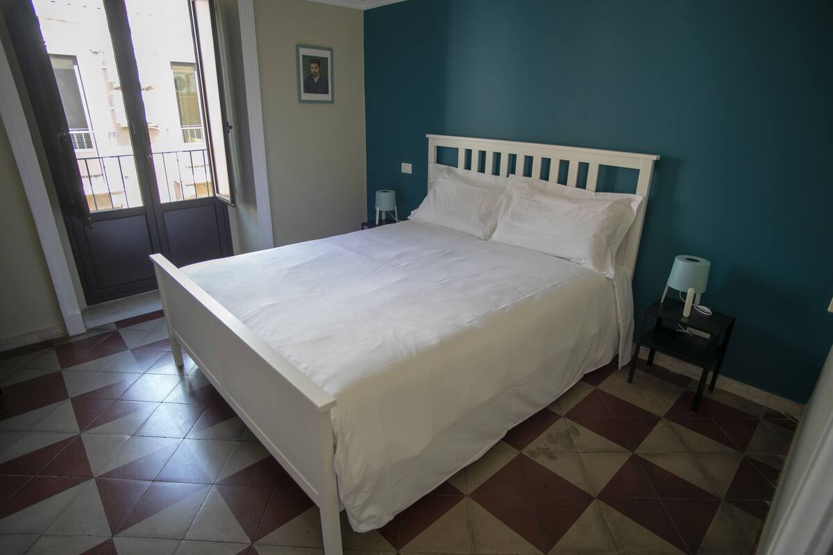 Een slaapkamer met een wit bed, blauwgroene wanden en een geruite vloer.