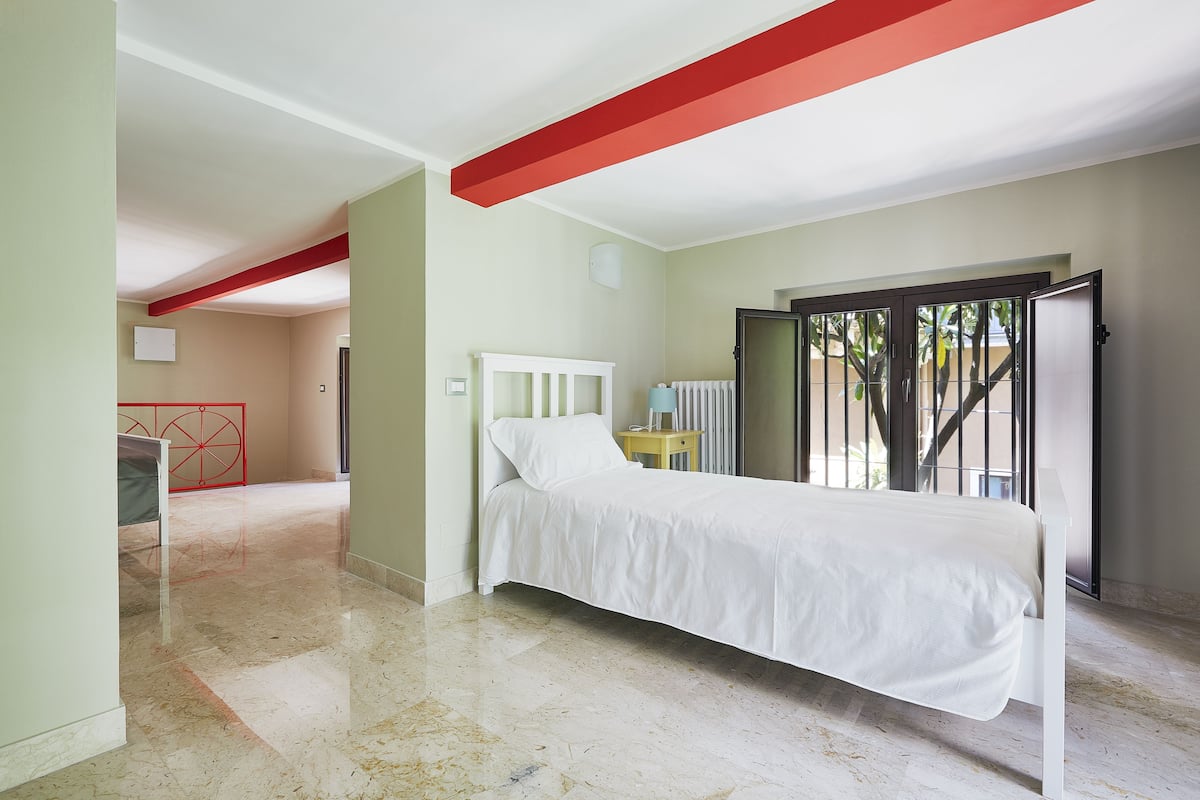 Een slaapkamer met een bed, een radiator, een raam met uitzicht en een deur naar buiten.