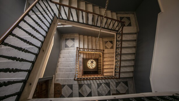 Un escalier avec une rampe en bois et un mur orné d’un motif géométrique.